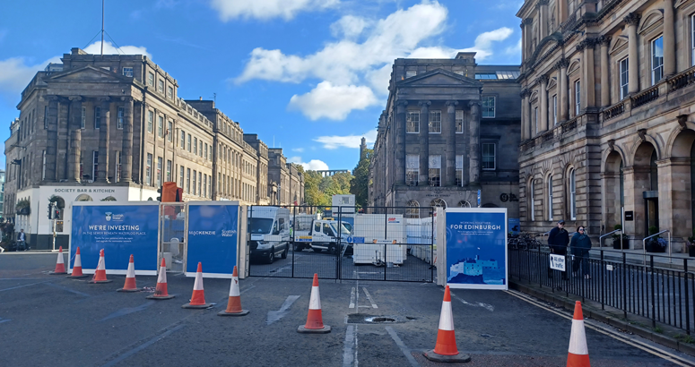 Traffic cones are shown in front of a city centre site compound