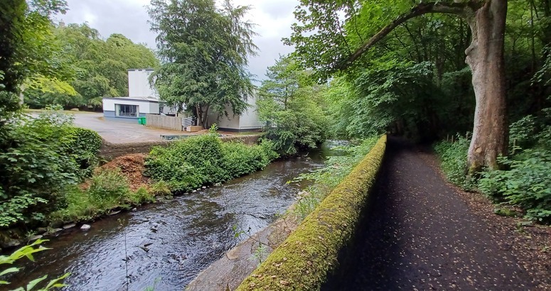 Image of muddy footpath with watercourse, car park and building to the left