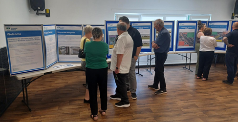 Members of the community are shown speaking to staff in front of information posters