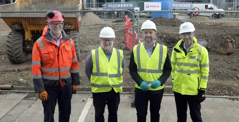 Four people in personal protective equipment stand outside a construction site
