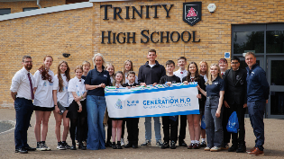 Group photo of students and staff standing outside Trinity High School holding a banner that reads 'Scottish Water - We won the Generation H₂O Making Waves Challenge'. Everyone is smiling and facing the camera.