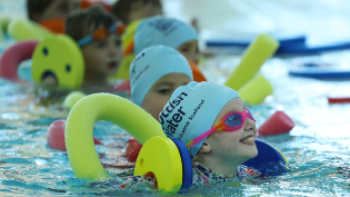 Children wearing Scottish Water Blue swimming caps use colourful pool noodles during a swimming lesson