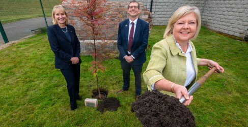 Three people smiling as one holds a metal spade covered in mud up to the camera