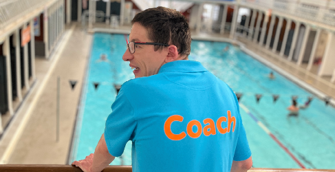 Scott Quin, wearing a blue shirt with 'Coach' written on the back, overlooking a swimming pool at Edinburgh Leisure's Leith Victoria facility.