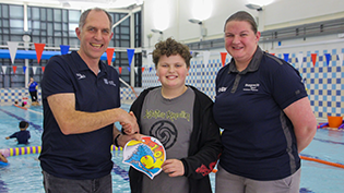 Scottish Swimming's Alan Reed with schoolboy Ruben Norbury with his winning cap design in centre and mum Jane on right at a swimming pool
