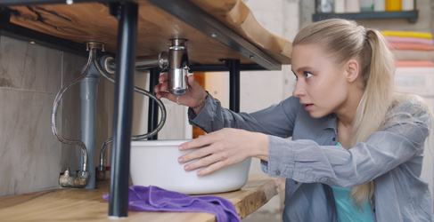 a woman holding a basin to fix a leak under a sink