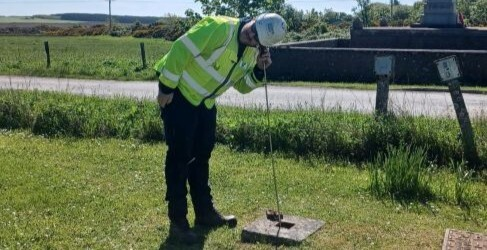 A Scottish Water male employee with a listening stick at a manhole